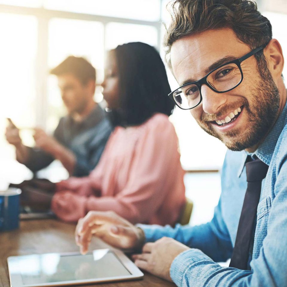 Male IT Professional wearing blue shirt and glasses smiling at computer