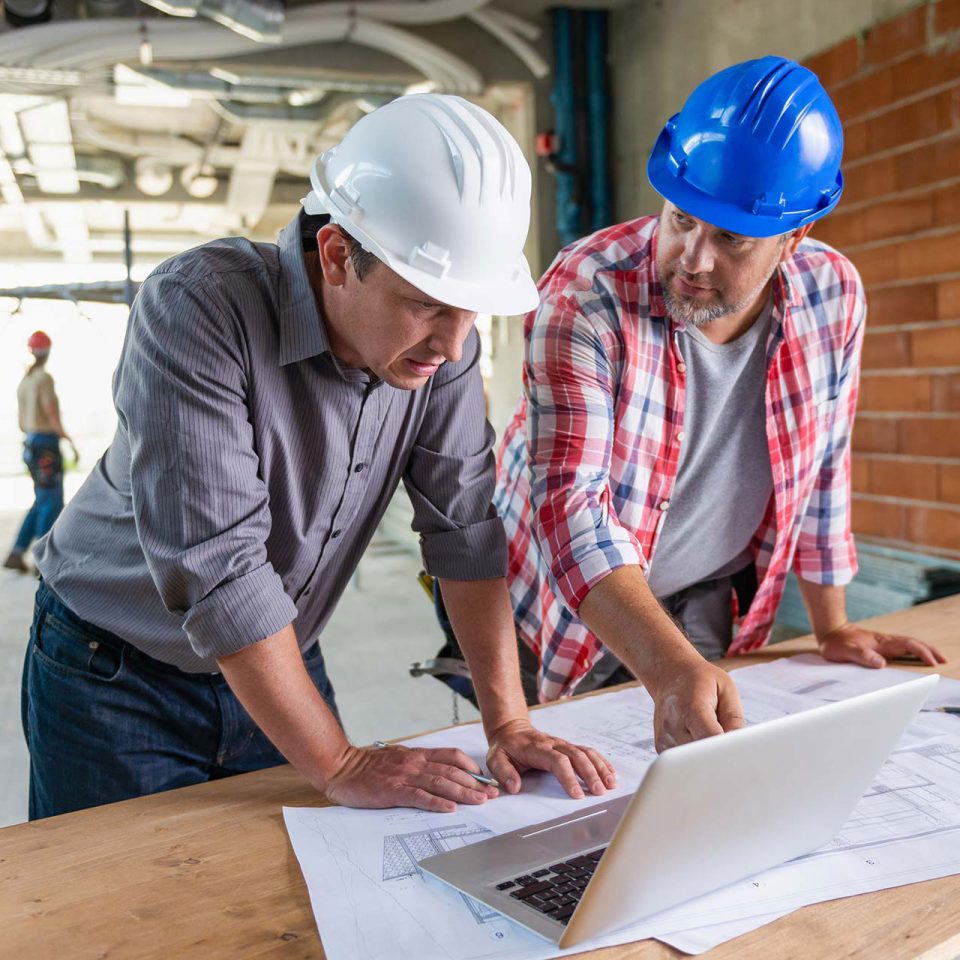 IT design professional in white hard hat and construction worker in blue hard hat review blueprint