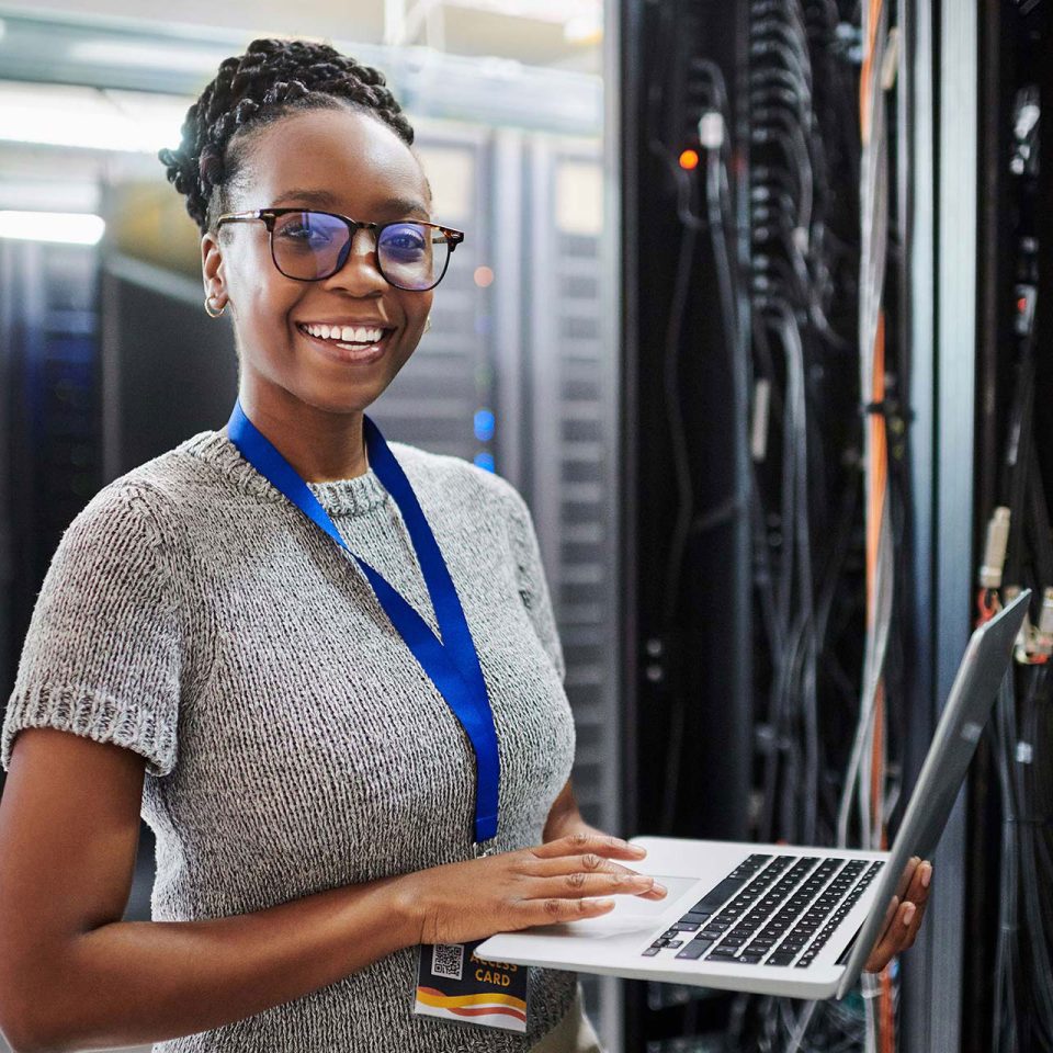 young African-American woman smiles in front of server room network