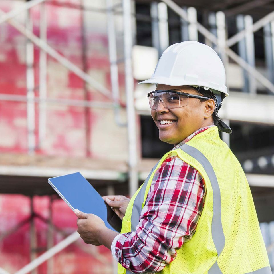 African-American woman working at construction site in safety goggles and white hard hat